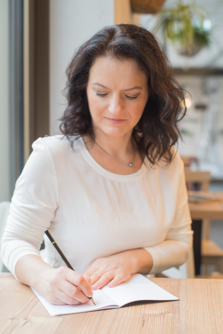 Sandra Brestrich bietet ein Marketing-Mentorin an. Auf dem Foto sitzt sie an einem Schreibtisch und notiert Infos in ein Notizbuch.