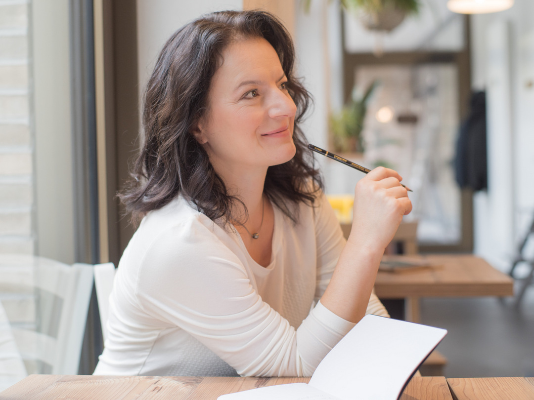 Sandra Brestrich sitz an einem Tisch. Sie schaut zur Seite und scheint einem Kunden in ihrem Marketing-Mentoring Programm zuzuhören.